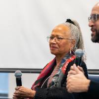 three people on stage, two at right hold microphones